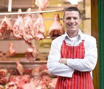 Butcher standing in front of butcher shop window